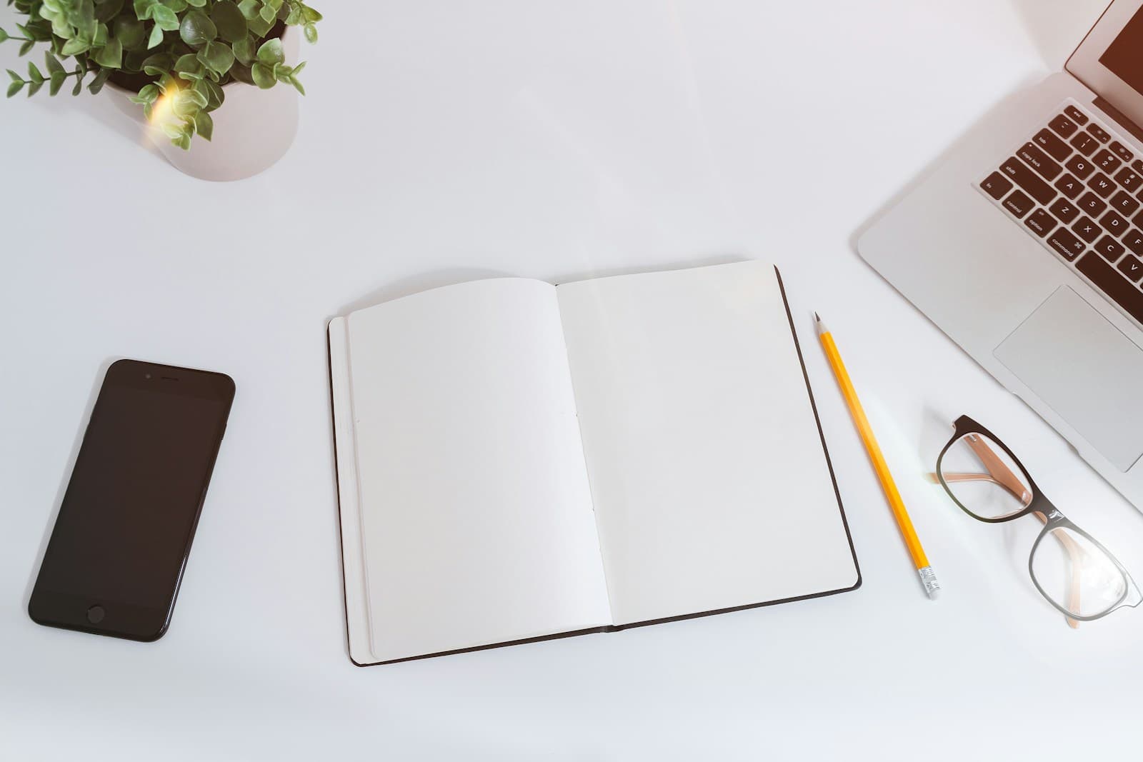 An open notebook beside a laptop on a white desk